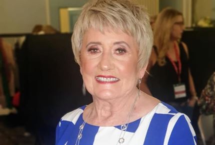 A photo of Anne smiling wearing a blue and white dress
