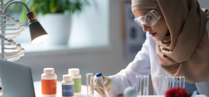 A young scientist wearing a headscarf and safety goggles working in a lab