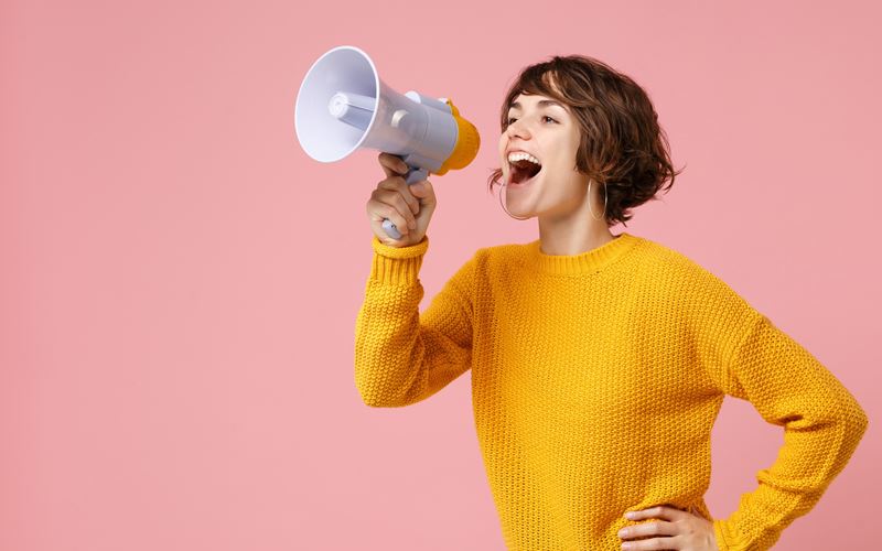 Woman in yellow jumper with megaphone on pink background