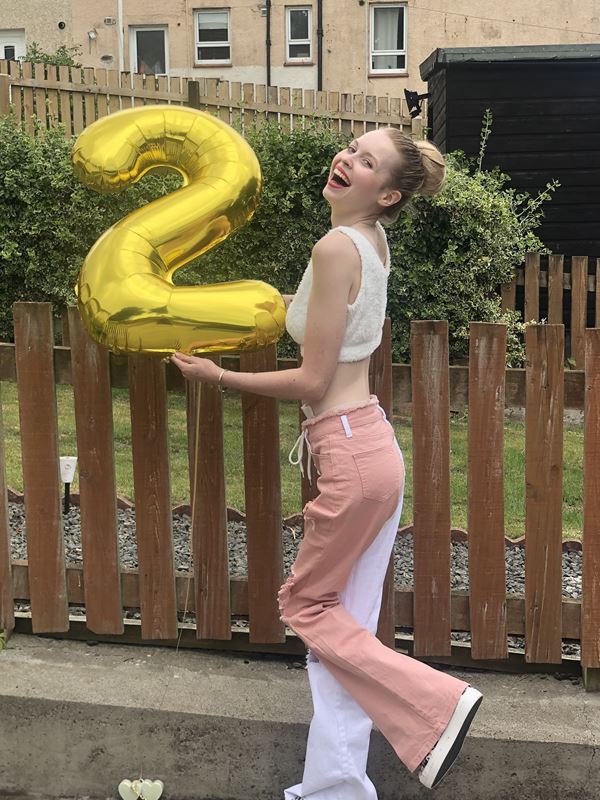 Eilidh smiling and holding a golden balloon in the shape of the number 2