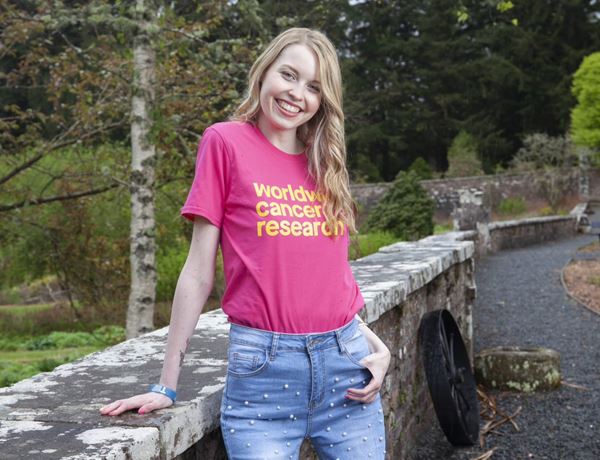 Eilidh standing outside smiling wearing a Worldwide Cancer Research tshirt