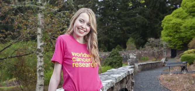 Eilidh standing outside smiling wearing a Worldwide Cancer Research tshirt
