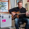 Singer Russell Watson playing guitar next to a silver record case with the Worldwide Cancer Research logo on