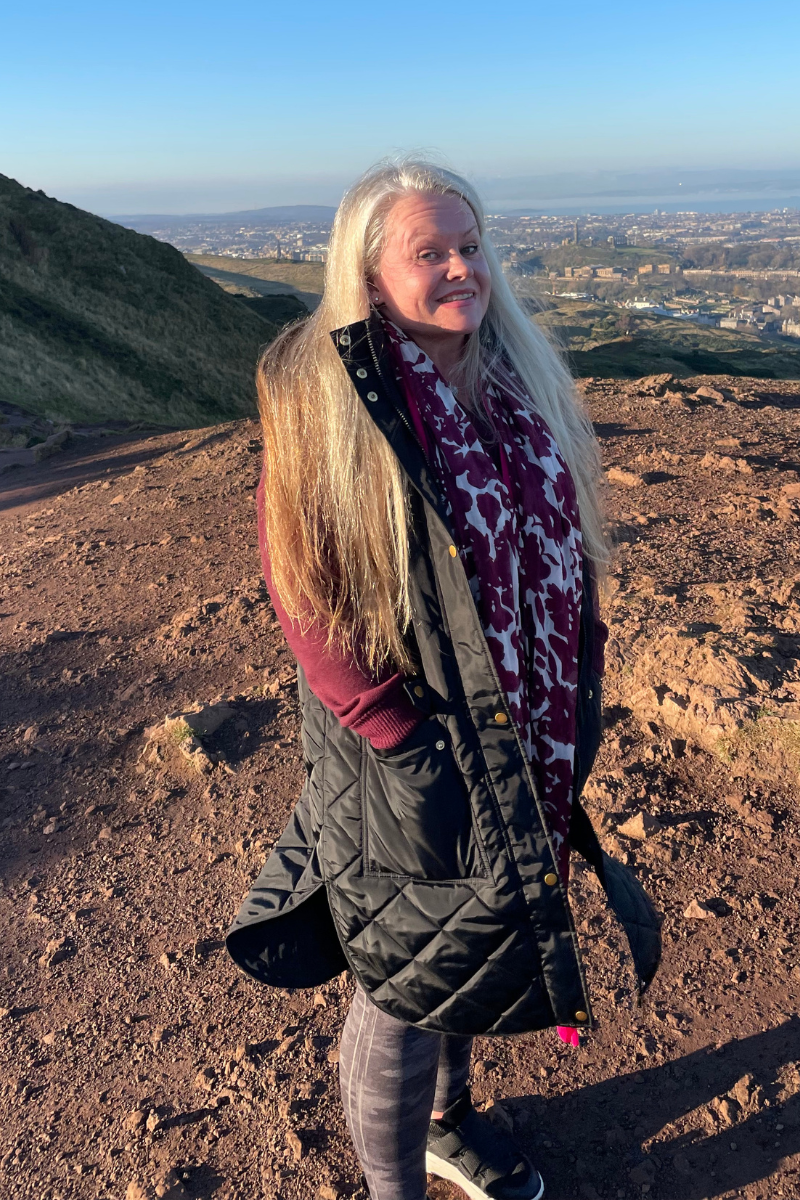 A full body photo of a woman with long blonde hair standing outside in the sunshine
