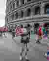 Picture of Run Rome The Marathon runner making a heart with her hands with other runners and the Colosseum behind her.
