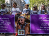 Seven women are pictured standing solemnly behind a banner raising awareness for lobular breast cancer, the urgent need for more funding, and a call to action for the British Government