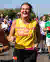 Female runner in a Worldwide Cancer Research t-shirt is laughing while looking at the camera and running by, on a beautiful sunny day.