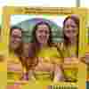 Three women wearing Worldwide Cancer Research t-shirts stand in a Worldwide Cancer Research selfie frame.