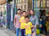 A woman and a man stand with two boys wearing yellow Worldwide Cancer Research t-shirts on a city street, smiling for the camera outside a shopfront.