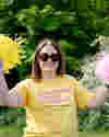 Smiling woman in sunglasses wearing a Worldwide Cancer Research t-shirt raises pom-poms to cheer.