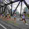 Runners in Toronto Marathon cross a bridge with Toronto skyline in the background.