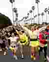 Runners in OC Half Marathon wave enthusiastically with lines of palm trees behind them.