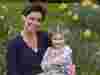 Victoria Robb and Matilda smile while sitting in a field surrounded by yellow flowers Matilda is holding a doll